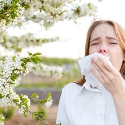 woman in the middle of sneeze with a tissue to her face, outdoors