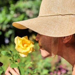 woman-wearing-sun-hat-smelling-yellow-rose