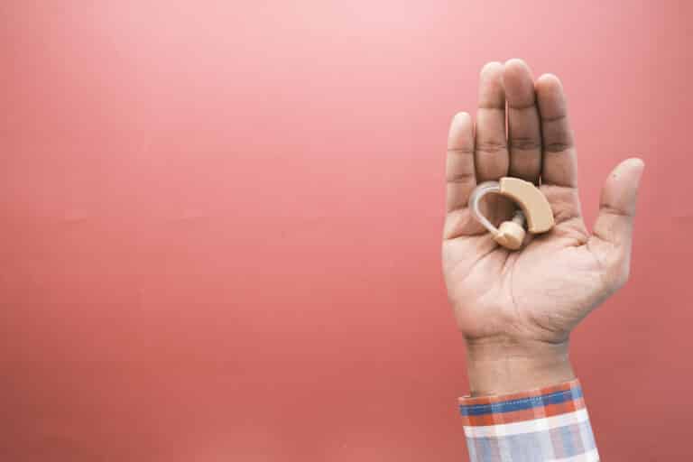 Hearing Aid Hand holding a hearing aid over a pink background