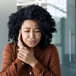 Woman experiencing uncomfortable ear pain, or ear stroke.
