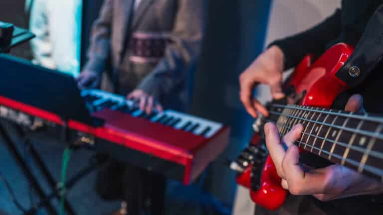 Close-up of hands playing electronic keyboard during live music performance with blurred bassist in background under blue lighting Close-up of hands playing electronic keyboard during live music performance with blurred bassist in background under blue lighting.