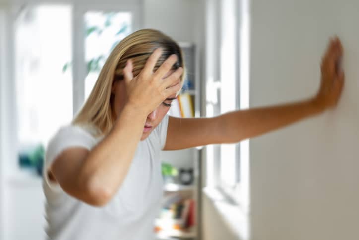 Woman With Tinnitus Woman Holding Head with Outstretched Arm Keeping Her Upright in Her Home Hallway