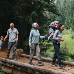 An active and happy multigenerational family hike across a small bridge, looking at the beautiful surrounding nature while bonding on a family camping vacation.