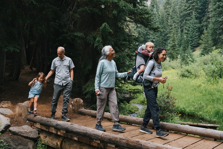 Multigenerational family on a hike An active and happy multigenerational family hike across a small bridge, looking at the beautiful surrounding nature while bonding on a family camping vacation.
